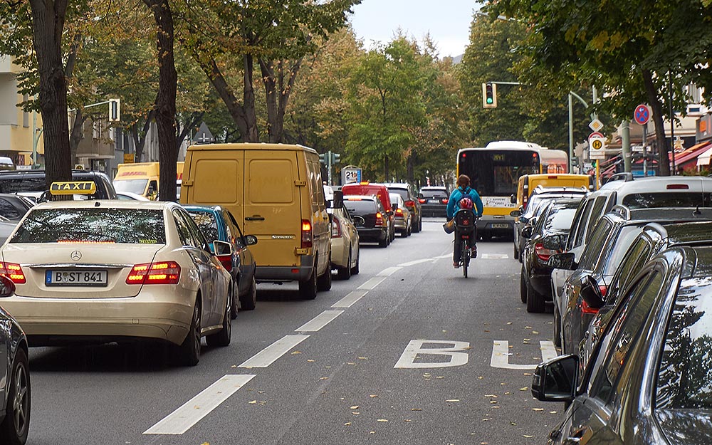 Foto: Frisch markierte Busspur mit parkenden Fahrzeugen und einer Radfahrerin.