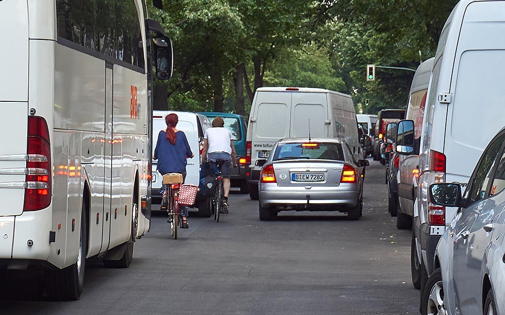 Foto: Radfahrer in der Sonnenallee zwischen in zweiter Reihe parkenden Fahrzeugen und dem fließenden Kfz-Verkehr.