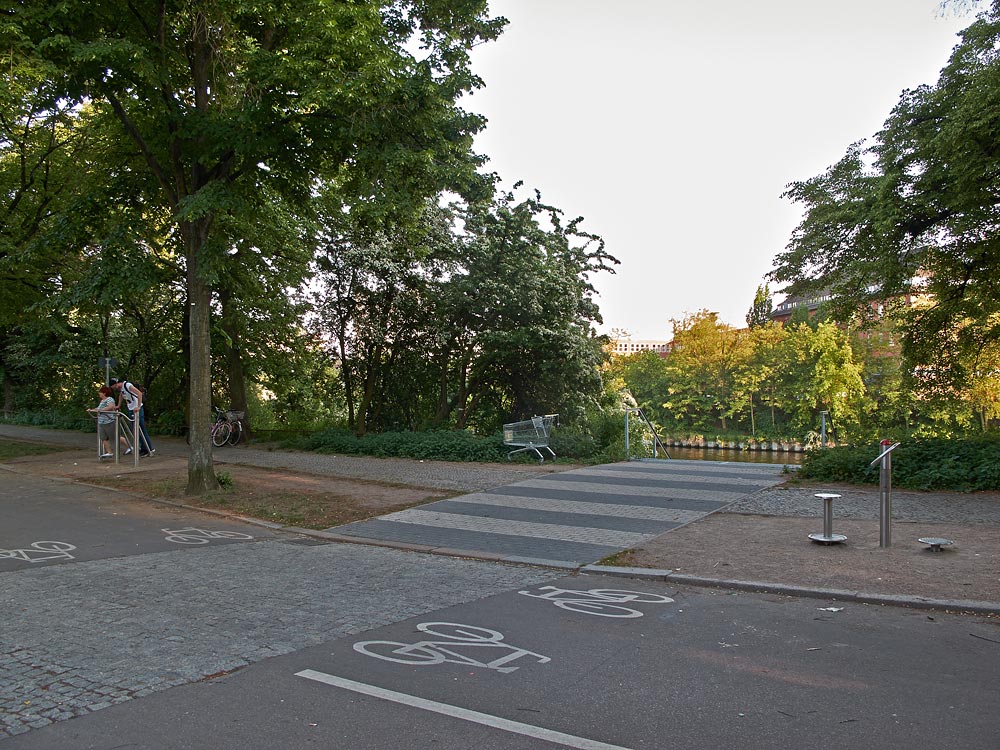 Foto: Durch Pflaster hervorgehobener Fußwegübergang über das Nordufer mit durch Fahrradsymbole gekennzeichneten Radstreifen.